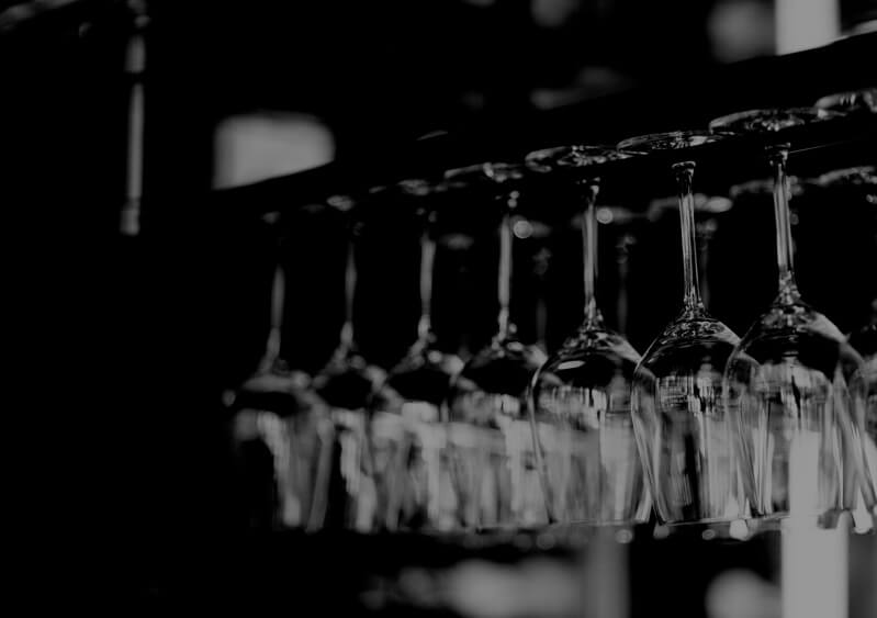 Black and white photo of wine glasses hanging from rack.