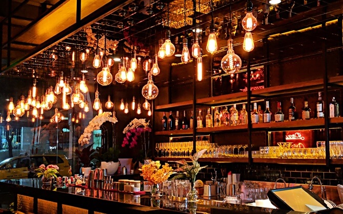 Vibrant display of lights hanging from the bar. Various alcoholic drinks and glasses are displayed behind bar.