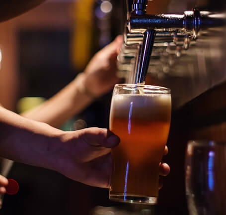 Photo showing a hand holding a beer glass while using a beer tap to fill up the glass with beer.