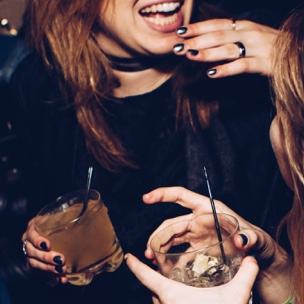 Zoomed in photo of two women laughing whilst holding alcoholic drinks.